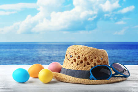 Easter eggs with hat and sunglasses on wooden table at shoreの写真素材