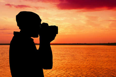 Silhouette of professional photographer taking photo of beautiful landscape during sunsetの写真素材
