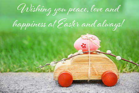 Greeting card design. Wooden toy car with pussy willow and Easter egg on grass backgroundの写真素材