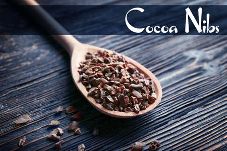 Aromatic cocoa nibs with spoon and text on wooden backgroundの写真素材