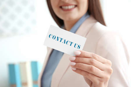 Young woman holding business card with text CONTACT US on blurred background. Recruitment conceptの写真素材