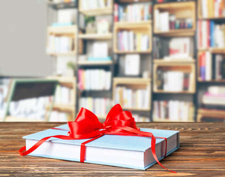 Book with ribbon bow as gift on wooden table at libraryの写真素材