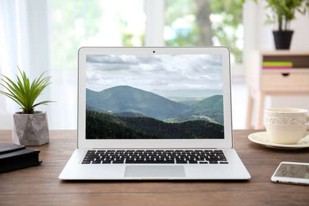 Workplace with laptop and wallpaper of landscape on screenの写真素材