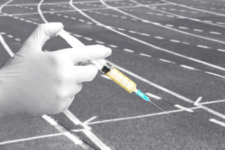 Scientist's hand in glove with syringe and running track on background, closeup. Sport and doping conceptの写真素材