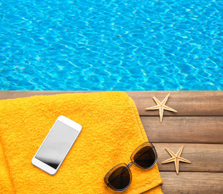 Beach set with smartphone for summer vacation on wooden pier near waterの写真素材