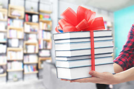 Woman holding books with ribbon bow as gift at libraryの写真素材