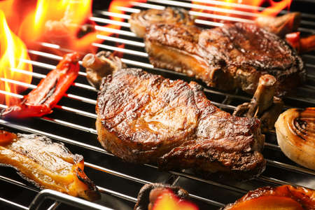 Delicious steak with vegetables on grilling grid and flame, closeupの写真素材