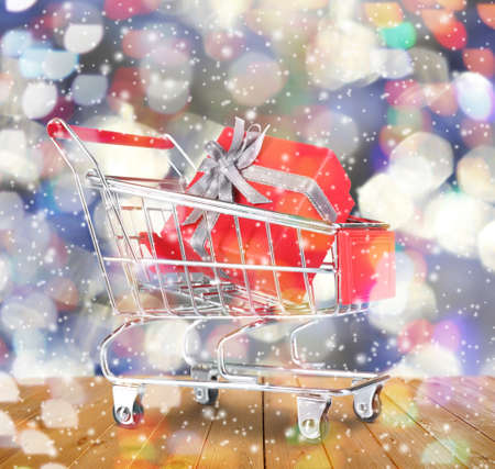 Shopping cart with gift on blurred lights background, snow effect. Boxing day conceptの写真素材