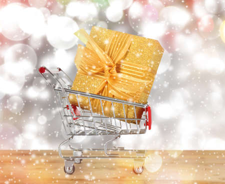 Shopping cart with gift on blurred lights background, snow effect. Boxing day conceptの写真素材