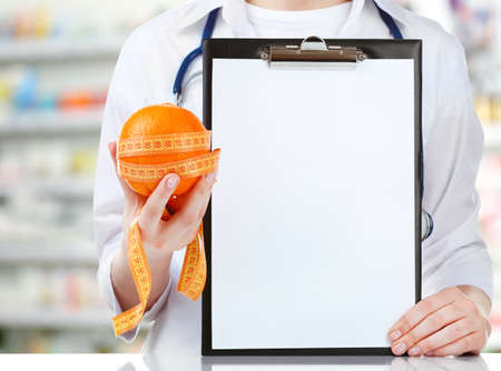 Nutritionist holding orange with measure tape and clipboard at pharmacyの写真素材