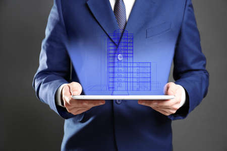 Real estate agent holding tablet and projection of building on dark backgroundの写真素材