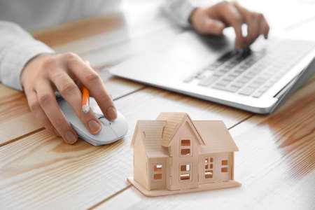 Real estate agent working with laptop and model of house on table in officeの写真素材