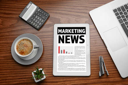 Tablet with cup of coffee and office stationery on wooden background. Marketing news on screenの写真素材