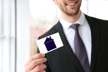 Real estate agent holding business card with drawing of house on blurred backgroundの写真素材