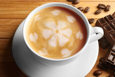 Cup of coffee latte art with grains and chocolate bar on wooden table, closeupの写真素材