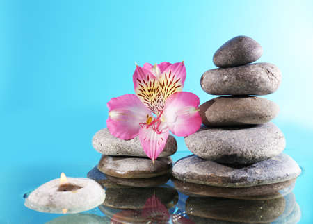 Stack of spa stones with flower and candlelight on blue backgroundの写真素材