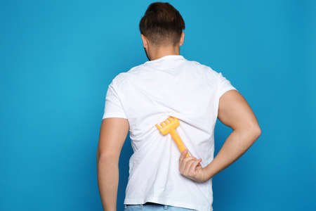 Young man scratching back with toy rake on color background. Annoying itch Young man scratching back with toy rake on color background. Annoying itch