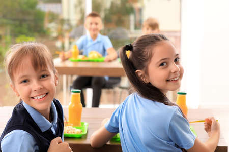 Happy girls at table with healthy food in school canteen Happy girls at table with healthy food in school canteen