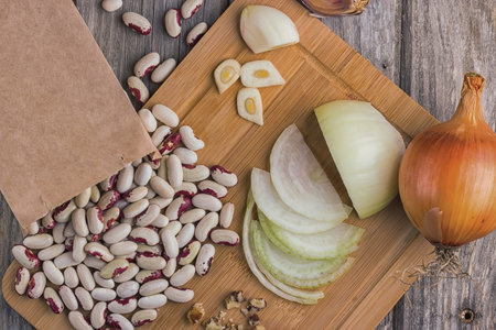 bean seeds in a paper bag, walnut kernel, onion, garlic on a wooden board