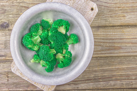 Fresh green broccoli in old metal bowl over rustic wooden desk on wooden background - healthy or vegetarian food concept Top view.の写真素材