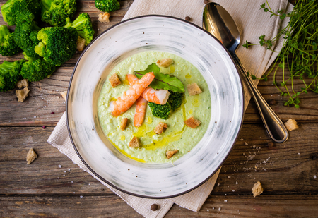 Broccoli green cream soup with shrimps in a plate on a rustic wooden background. Clean food, healthy diet concept. Tasty food. Top view, flat lay.の写真素材