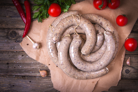 Raw fresh white sausages on a craft paper with vegetables. Weisswurst in a heap. Traditional Bavarian or Munich white sausage made from sliced veal and pork bacon. Oktoberfest concept.の写真素材