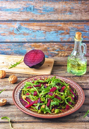 Spring detox salad salad with arugula and boiled beets with walnut kernel and roasted sesame seeds, poured with olive oil in a rustic ceramic plate on a wooden background, top view.の写真素材