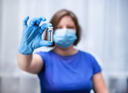 A woman doctor in gloves and a medical mask, holds an ampoule with a medicine in her hand.