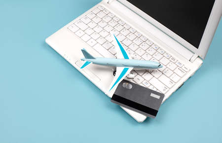 White laptop on a blue background. Nearby is a bank card and a miniature airplane. Concept - Online booking of air tickets, travel planning. Payment for orders via the Internet.の写真素材