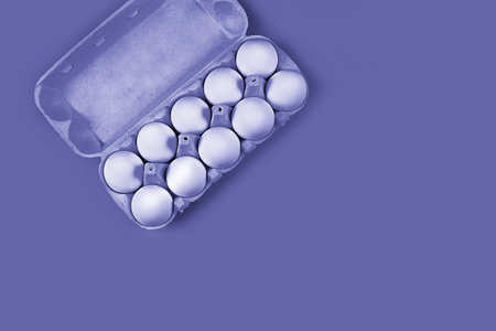 White chicken eggs, 10 pieces in a cardboard box in the upper left corner on a very peri lavender...