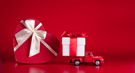 Red car with a gift box on a red background. Concept - delivery of gifts for the holidays,...