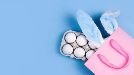 Wide banner on a blue background. The concept of online shopping for Easter, purchases and sale for the holiday. Gift bag with bunny ears and Easter eggsの写真素材