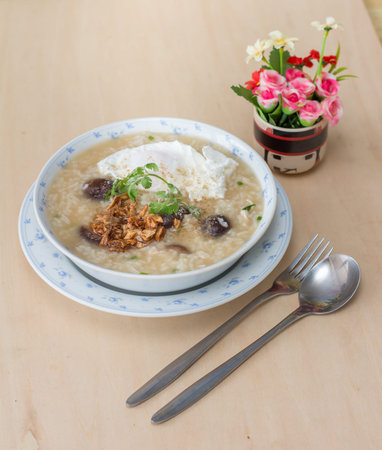 Rice porridge with garlic and egg breakfast in white bowl on wooden table
