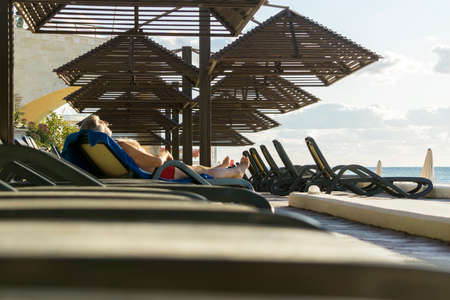 an elderly man is resting lying by the sea on a sun lounger, a resort area with sun loungers and wooden sun umbrellas. Sunny summer day.の写真素材