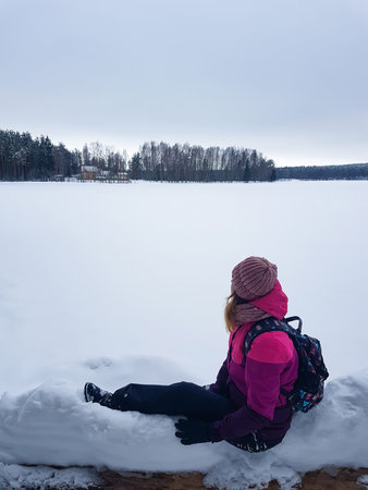 Young traveling girl standing in front of beautiful mountain lake. Winter is coming, first snowfall....