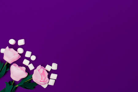 Three pastel roses with scattered little marshmallows lie on a bright purple background. View from above. Copy space.の写真素材