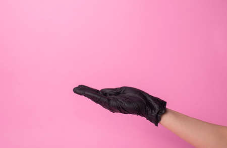 hand in black gloves of doctor or hair stylist on pink background. gloves are worn on the arm.の写真素材