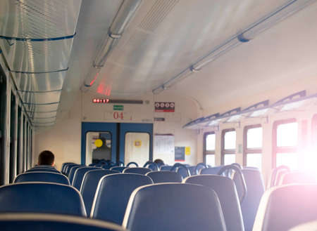 Rows of blue soft seats in a passenger train car. Bright sun shines through the window.の写真素材
