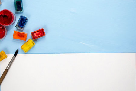 Brush, watercolor paint and sheet of paper on a blue background. Place for text. Top view with copy...