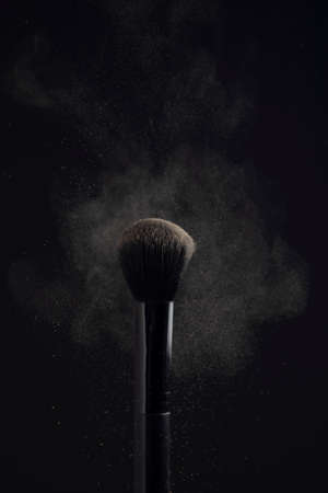 powderbrush with cloud of face powder on black background.の写真素材