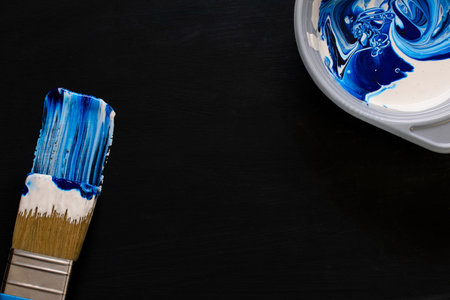 paint brush painting with blue color. in the upper corner is a plate with mixed white and blue colors. close-up. dark background. copy space. flat layの写真素材