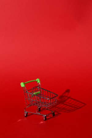small empty metal trolley from a supermarket on a red background. Hard directional light, clear shadow from the cart. Horizontal photo. Place for text. trading conceptの写真素材