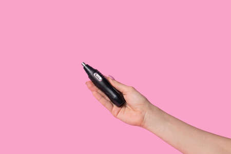 Female hands gently hold a male black electric trimmer. Minimalism on a pastel pink backgroundの写真素材