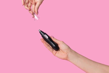 Female hands gently hold a male black electric trimmer. Minimalism on a pastel pink backgroundの写真素材