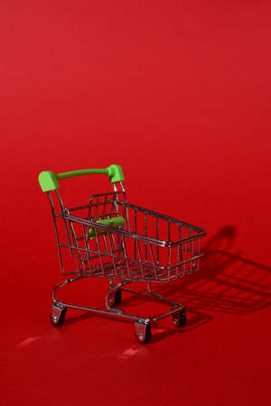 small empty metal trolley from a supermarket on a red background. Hard directional light, clear shadow from the cart. Horizontal photo.trading concept.の写真素材
