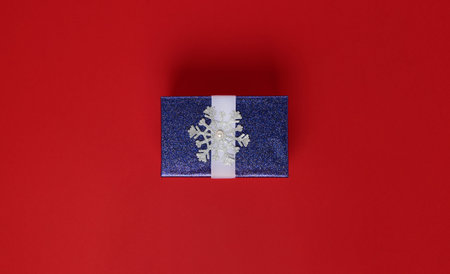 Gift box in the center of the frame on a red background. A box of blue in sparkles and with a...