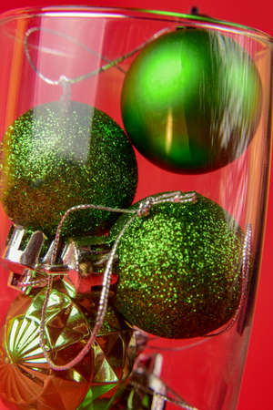 little green christmas balls lie inside a glass of champagne on a red background. Close-up.の写真素材
