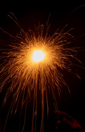 sparkler in hand on a black background. Long bright sparks fly in different directions. Long...