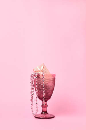 pink wine glass on a pastel pink background. Beads and a gift box are in the glass. All objects and background are in pink color. Minimalism. Copy space.の写真素材
