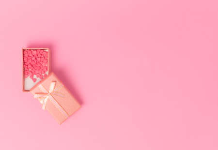 pink gift with a bow in the center of the frame on a pink background. view from above. Little sweet candy hearts lie inside a gift box. copy spaceの写真素材